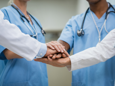 Healthcare team placing hands together in a show of teamwork and support in a clinical setting