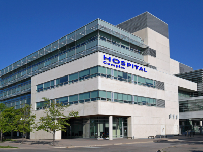 Exterior of a modern hospital building with glass windows, a prominent blue 'HOSPITAL Careplex' sign, and a visible entrance under a clear blue sky.